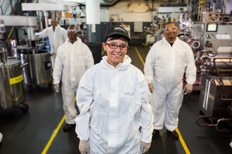 NUtec Digital Ink's first female ink milling technician smiling in a manufacturing facility with colleagues, showcasing diversity and expertise in digital printing ink production.